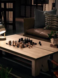 A modern living room featuring a wooden table with a chessboard and wooden figurines, surrounded by a brown leather sofa with