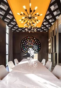 A modern dining room with a long marble table and chairs, industrial-style chandelier, and abstract wall art of a woman with