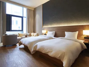 A modern, minimalist hotel room featuring wooden furnishings and fabric bedding.