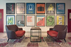 Modern office space with two brown armchairs, a wooden table, and colorful posters on the wall.