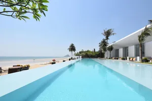 A modern residential swimming pool with glass walls and a view of the beach.