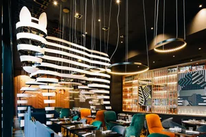 A modern restaurant interior with hanging lights, colorful chairs, and glass-fronted shelves.