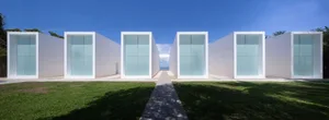 Minimalist architectural design featuring large white glass windows with a paved walkway and green lawn.