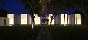A minimalist architectural building exterior at night, illuminated by interior lights.