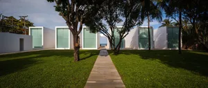 A minimalist modern house with white concrete walls and large glass windows surrounded by lush greenery and a neatly maintain