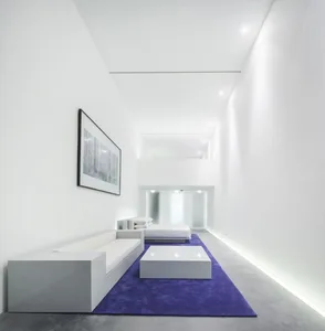 A minimalist living room with white furniture and concrete flooring.