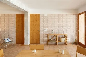 A cozy and modern interior space featuring wooden doors, tables, and chairs with a patterned wall and terracotta floor tiles.