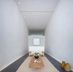 A minimalist living room featuring a concrete floor, a low wooden coffee table, and a white sofa.