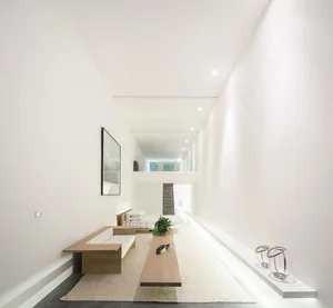 Modern minimalist living room with a white interior featuring a low-slung sofa, a long low coffee table, and a glass wall.