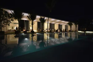 Evening view of a modern residential building with glass walls, concrete structure, and palm trees.