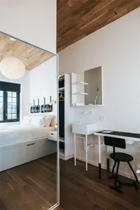 A minimalist bedroom with a white bed, wooden floor, and wooden ceiling.