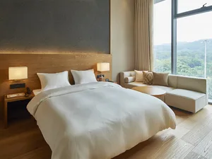 A minimalist residential bedroom featuring a neatly made bed with a wooden headboard and a comfortable sofa with cushions in 