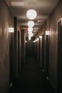 極簡酒店走廊，混凝土牆面，由球形吊燈與房間號碼牌照亮。