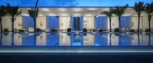 A modern residential exterior featuring a glass poolside with palm trees at dusk.