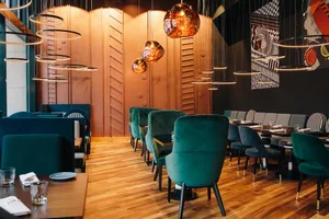 Modern restaurant with metallic texture on walls and ceiling, green velvet chairs, and circular hanging lights.