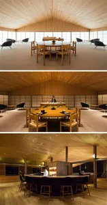 Modern restaurant interior with wooden tables and chairs, large windows, and a high wooden ceiling.