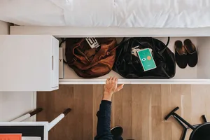 Hand reaching into wooden drawer with books, bags, and shoes inside