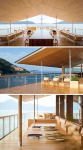 A modern residential interior featuring a wooden ceiling, large windows overlooking the water, and a communal dining area wit