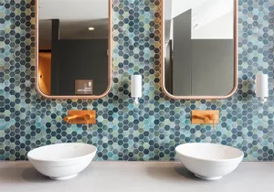 Modern bathroom with two white sinks, blue hexagonal tiles on the wall, and two rectangular mirrors.