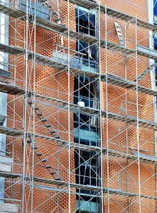 Steel scaffolding frames surrounding an unfinished brick building under construction.
