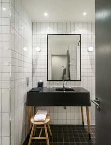 Industrial-style bathroom with white tiled walls, a concrete countertop, and a wooden stool.