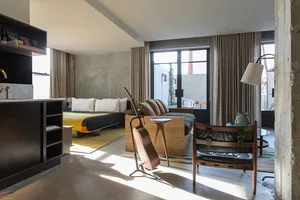 Modern, industrial-style bedroom featuring concrete walls and flooring, with minimalist furnishings and a guitar