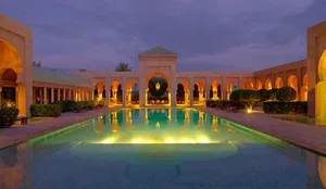 A beautifully illuminated outdoor pool with marble flooring and surrounding arches.