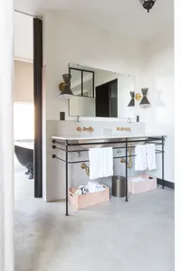 A modern bathroom with concrete flooring, white tiled walls, and a metal sink stand with a glass counter.
