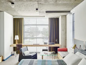 A contemporary bedroom featuring concrete walls, glass windows, and upholstered furniture.