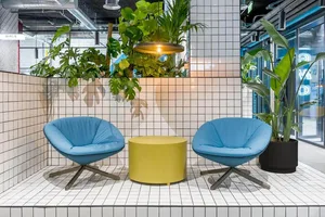 Modern coffee shop with blue fabric chairs on tiled floor, featuring a yellow central table and industrial-style light fixtur