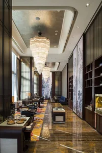 Modern hotel lobby with marble flooring, chandeliers, and seating arrangements.
