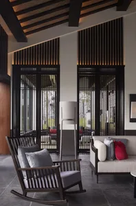 Modern living room featuring contemporary furnishings with wooden rocking chair, metal sofa, and glass elements.