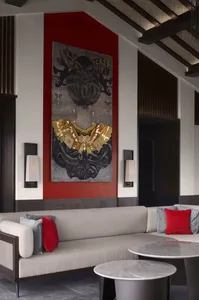 Modern lounge area featuring a beige sofa with red and gray cushions and a large, mixed-media art piece on the wall.