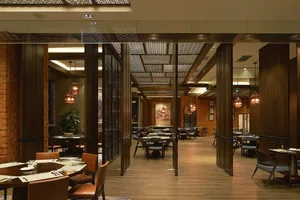 A contemporary restaurant interior with wooden tables, brick walls, and glass pendant lights hanging above round tables.