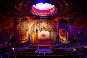 A grand theater stage adorned with ornamental cast-iron decorations and a luminous circular ceiling light.