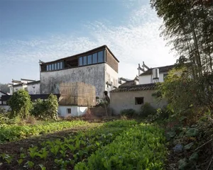 A traditional residential home with concrete walls, wooden structures, and a garden with green plants and vegetables.