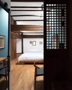 Modern minimalist bedroom featuring a white bed and wooden elements, with a view of the ceiling beams.