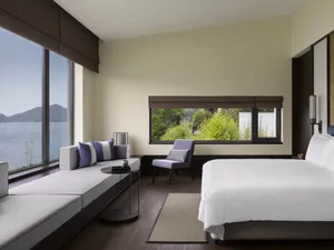A minimalist bedroom featuring a large window with a view of lush greenery and water.