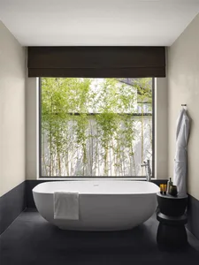 Modern, minimalist bathroom featuring a freestanding bathtub with a concrete tile floor and large window overlooking bamboo p