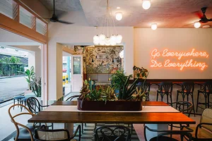 Modern cafe interior featuring sea glass mosaic tile accents, wooden tables, and potted plants.