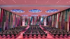 Large conference hall with rows of tables and chairs, illuminated by colorful textiles on the walls and ceiling lights.