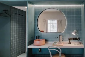 Industrial-style bathroom featuring blue tiled walls and floor, a pink sink, and a round mirror.