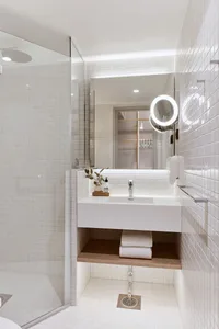 White-tiled bathroom with minimalist design, featuring a sink, shower, and towel storage.