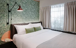 A minimalist hotel room with a bed featuring white cotton bedding, lace curtains, metal headboard, and glass window.