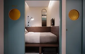 Modern hotel room with a bed, concrete walls, and a lighting fixture.