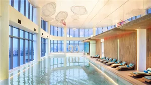 A minimalist indoor swimming pool with glass walls and a cloud-shaped light fixture.