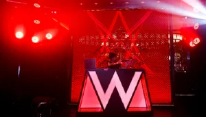 A DJ booth with a red light display and a large W logo in front of a red textured background.