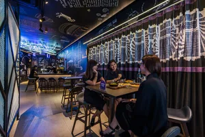 Three women sitting at a table in an industrial-style restaurant with metal, glass, and concrete elements.