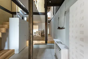 A minimalist small-space interior featuring concrete walls, wooden stairs, and metal accents.