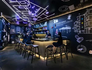 A stylish, modern bar counter with black metallic surfaces, illuminated by purple and blue neon lights, featuring intricate w